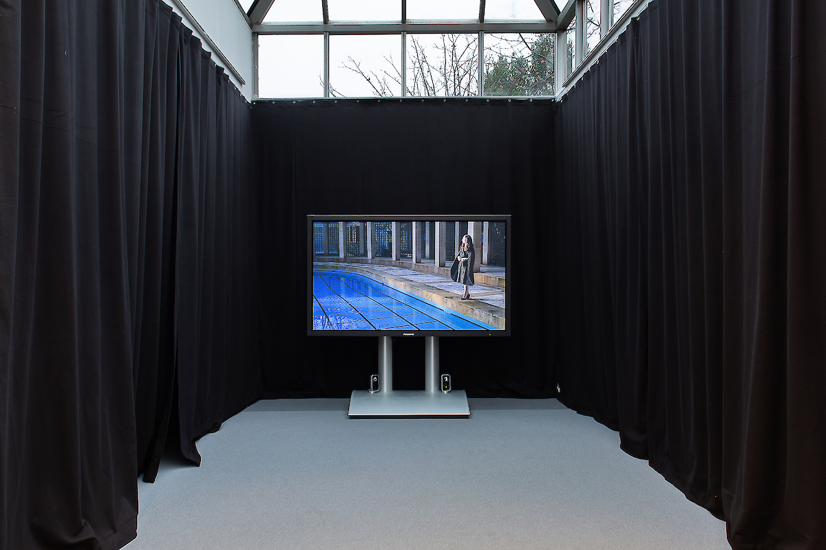 Un écran géant allumé au fond d'une salle dont les murs sont recouverts de tenture noire
