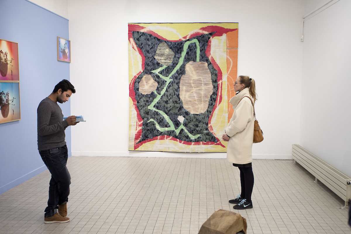 tapisserie accrochée au mur et deux personnes qui regardent les œuvres