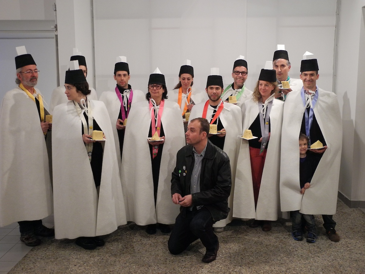 Des personnes portant un uniforme de la confrérie du fromage avec un plateau de fromage