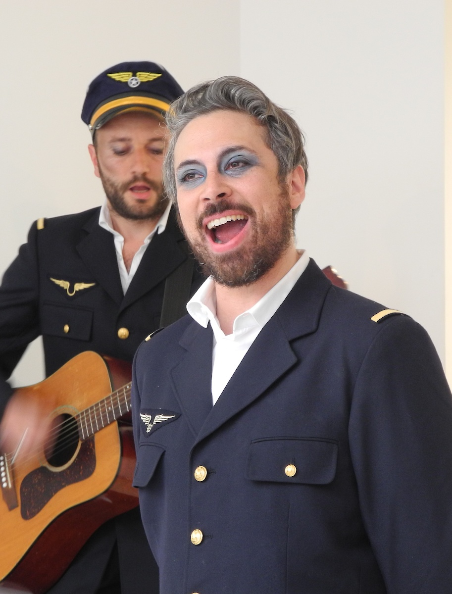 Un homme habillé en pilote de ligne maquillé en bleu chante