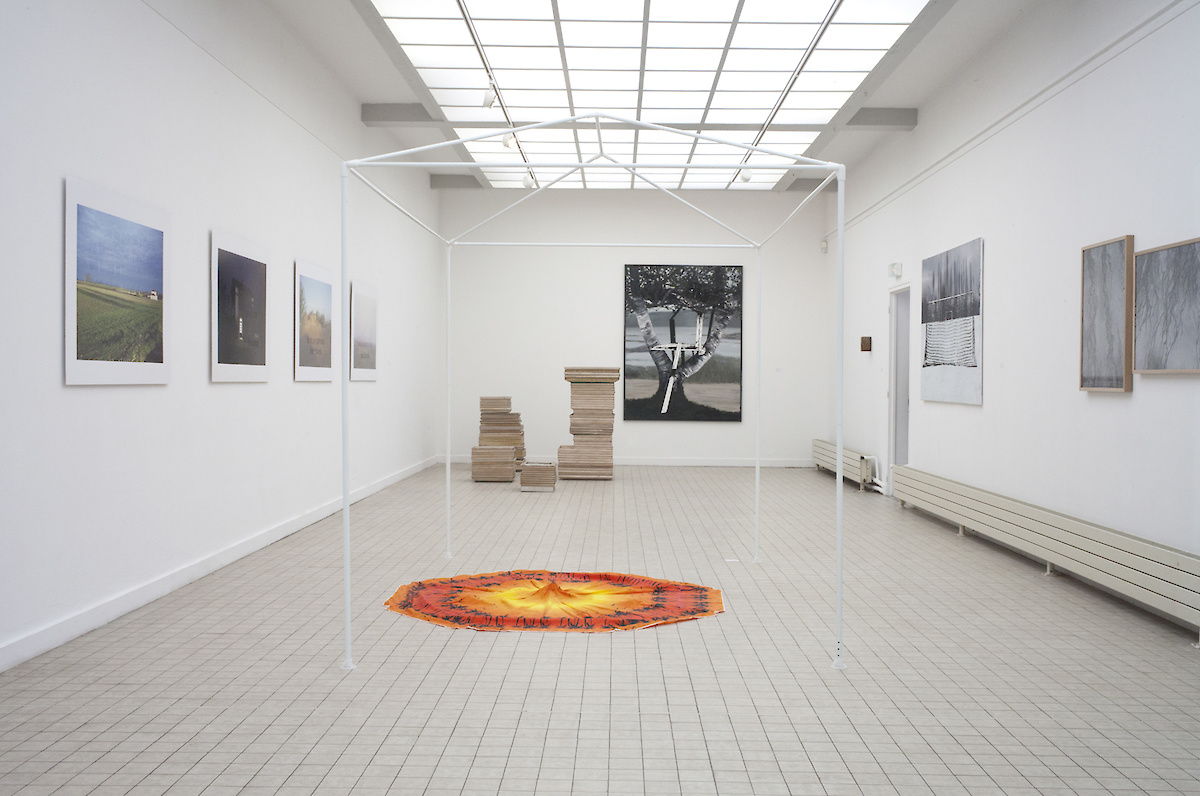 Vue de l'exposition : un tapis orange, des tableaux au mur