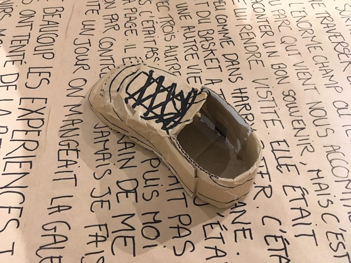 Une chaussure en carton posé sur une plaque de carton sur laquelle un texte est écrit
