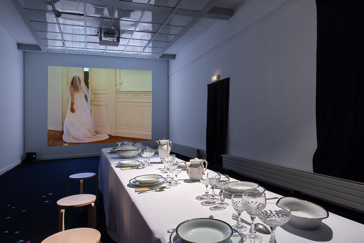 Une table dressée. Sur un écran, une mariée tourne le dos